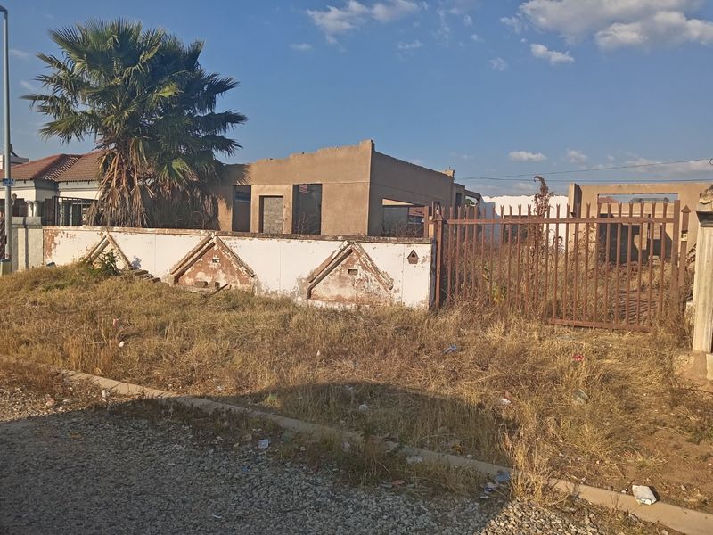 Vacant residential plot featuring an unfinished building structure, perimeter boundary wall, and metal gate, requiring significant site clearance and development.
