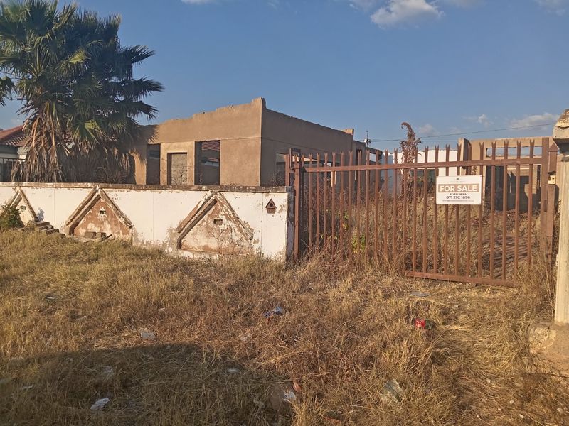 Vacant residential plot featuring an unfinished building structure, perimeter wall, and metal gate, offering potential for redevelopment or completion.