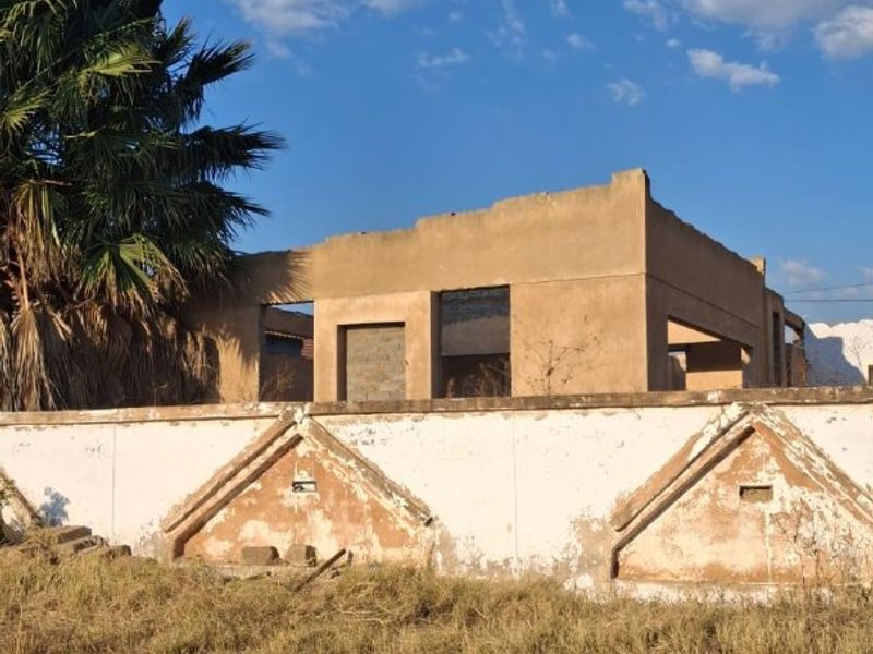 A view of a vacant residential plot featuring a dilapidated boundary wall and the shell of an unfinished building structure.