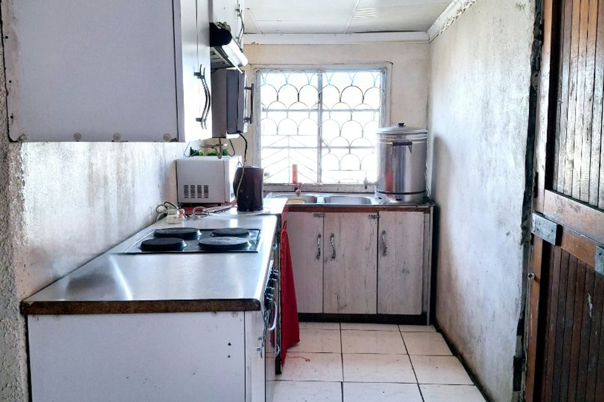 A compact kitchen featuring basic cabinetry, an electric hob, and tiled flooring, requiring significant cosmetic updates and refurbishment to modernize the space.