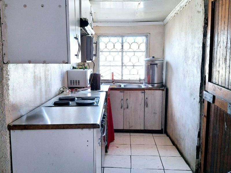 A compact kitchen featuring basic cabinetry, an electric hob, and tiled flooring, requiring significant cosmetic updates and refurbishment to modernize the space.