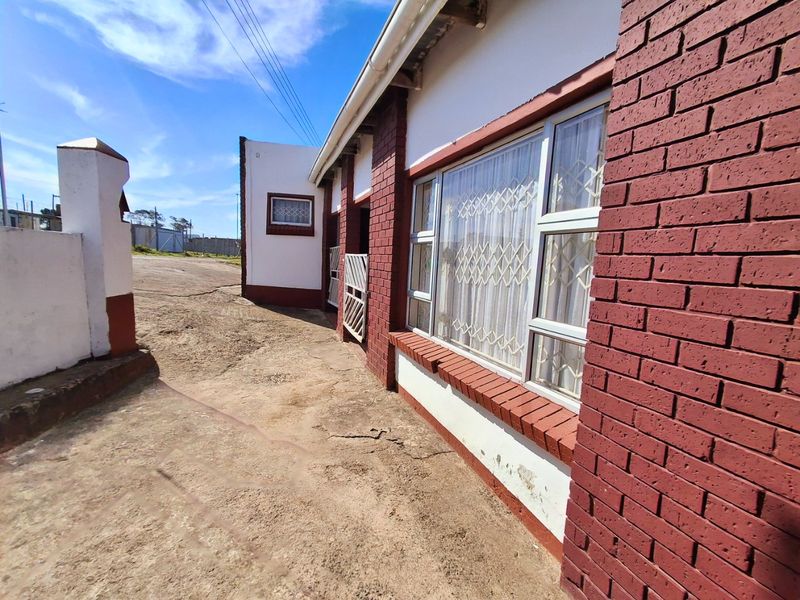 Side view of the property featuring red brick facade, security gates, and aluminium window frames, with visible wear on the exterior paint and driveway.