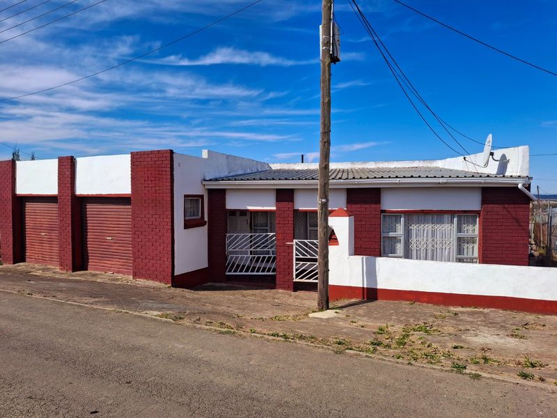 Front elevation of a single-story brick house featuring a roller shutter garage, security gates, and a corrugated metal roof.