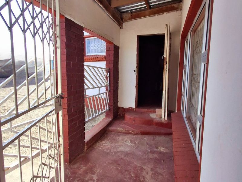 A covered outdoor patio area featuring exposed timber rafters, brick pillars, and a security gate, providing access to the main entrance.