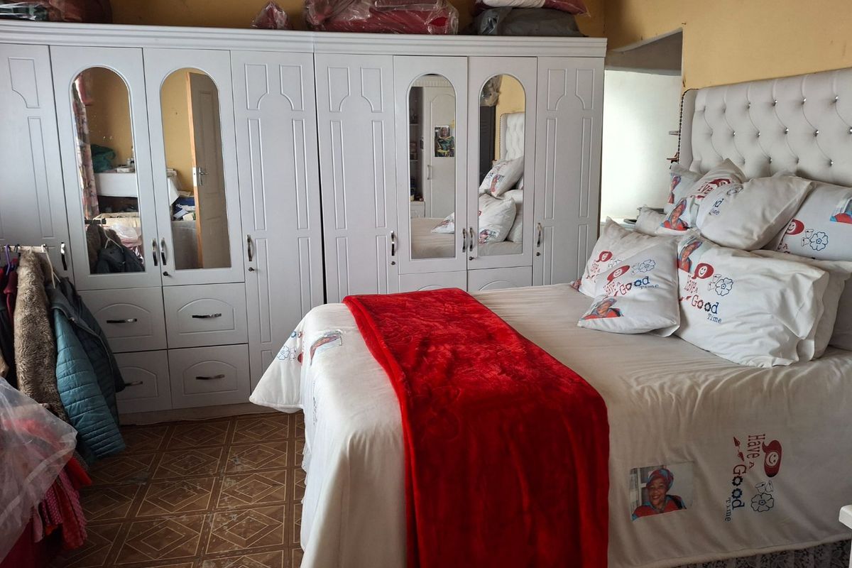 A bedroom featuring a large white built-in wardrobe with mirrored panels and tiled flooring.