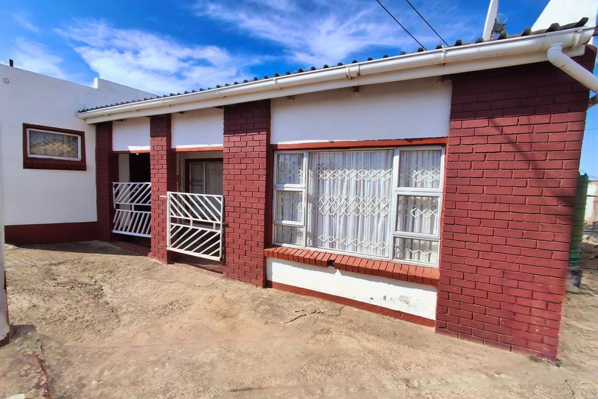Rear exterior view of the house featuring red brick facade, security gates, and aluminium windows with a concrete paved area.