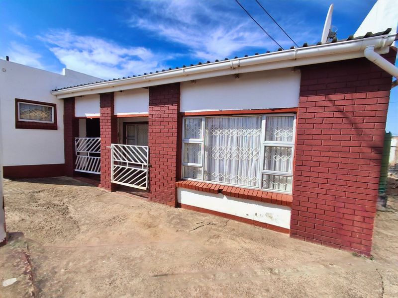 Rear exterior view of the house featuring red brick facade, security gates, and aluminium windows with a concrete paved area.