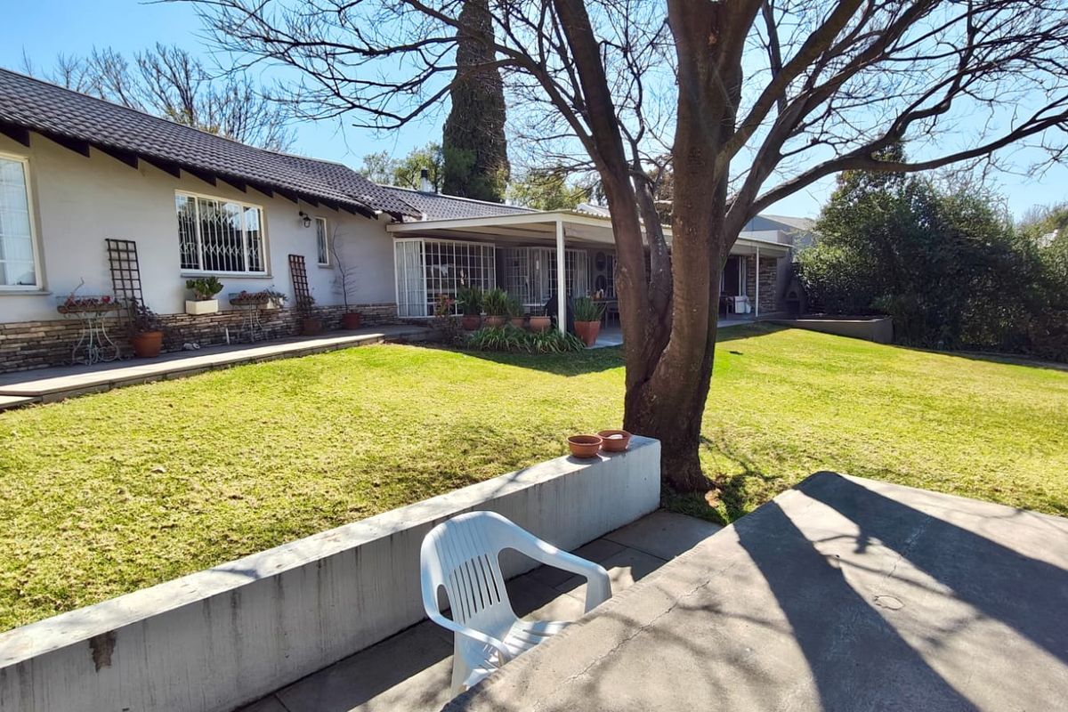 Rear view of the house featuring a spacious lawn, a covered patio area, and stone-clad exterior walls.