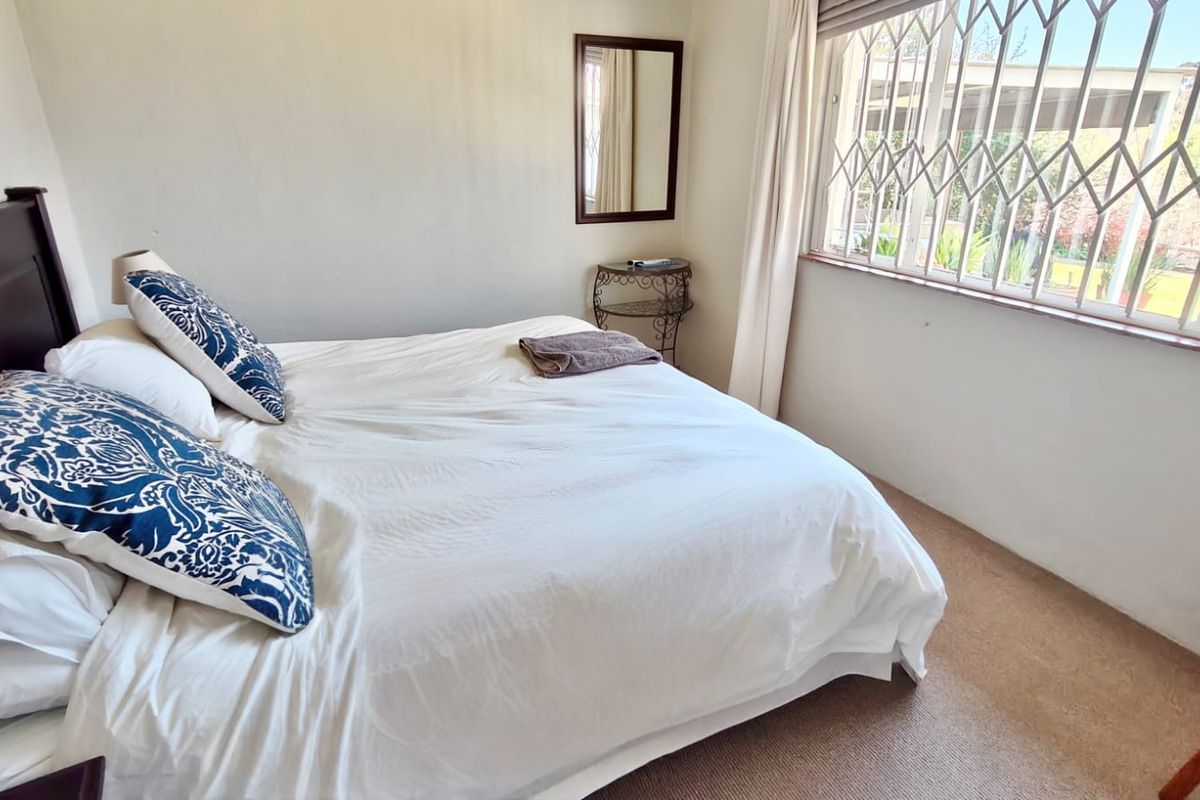 A functional bedroom featuring carpeted flooring and a window fitted with a security gate, providing natural light and basic security.