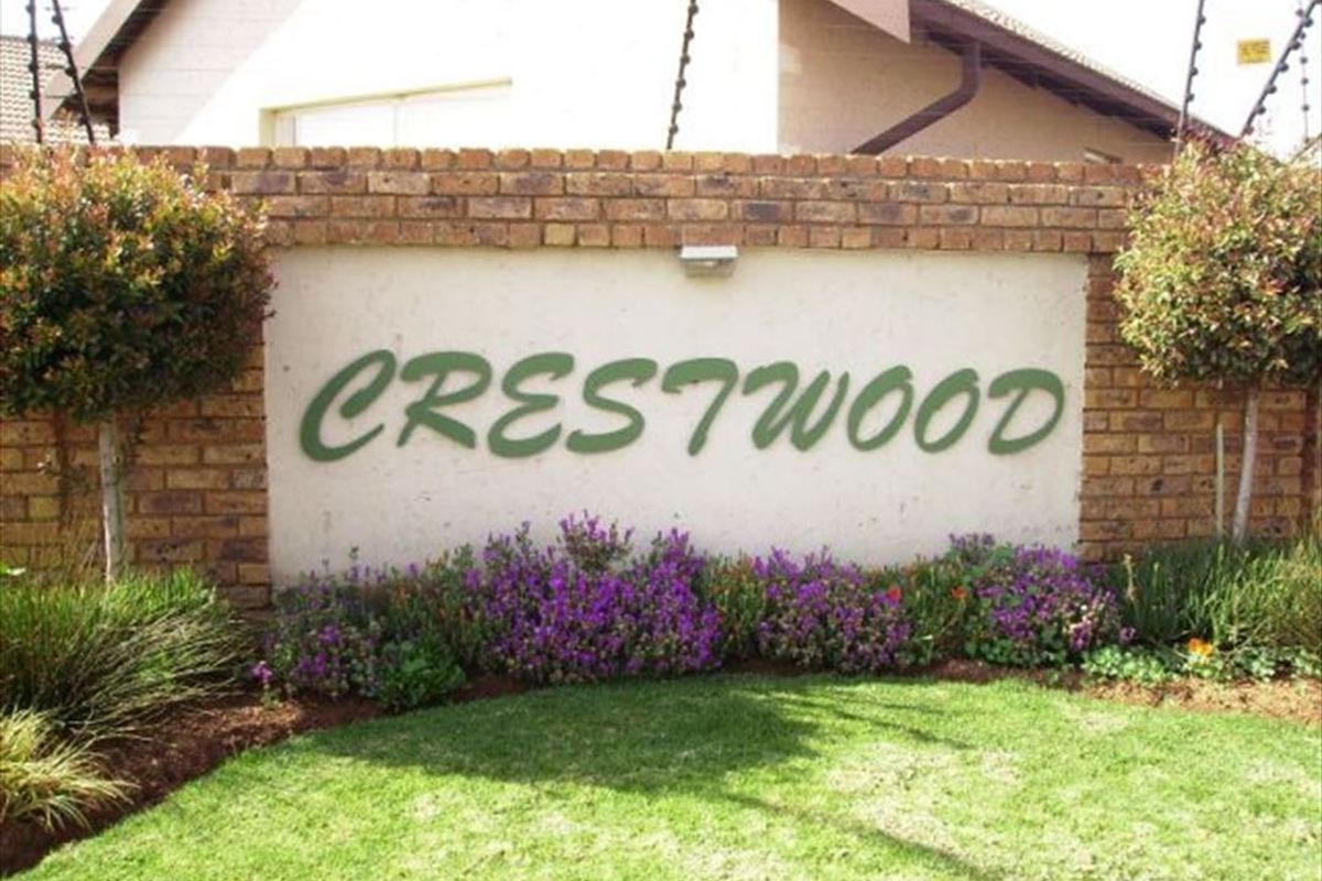 The entrance signage and landscaped front garden of the Crestwood townhouse complex, featuring a brick boundary wall and integrated security fencing.