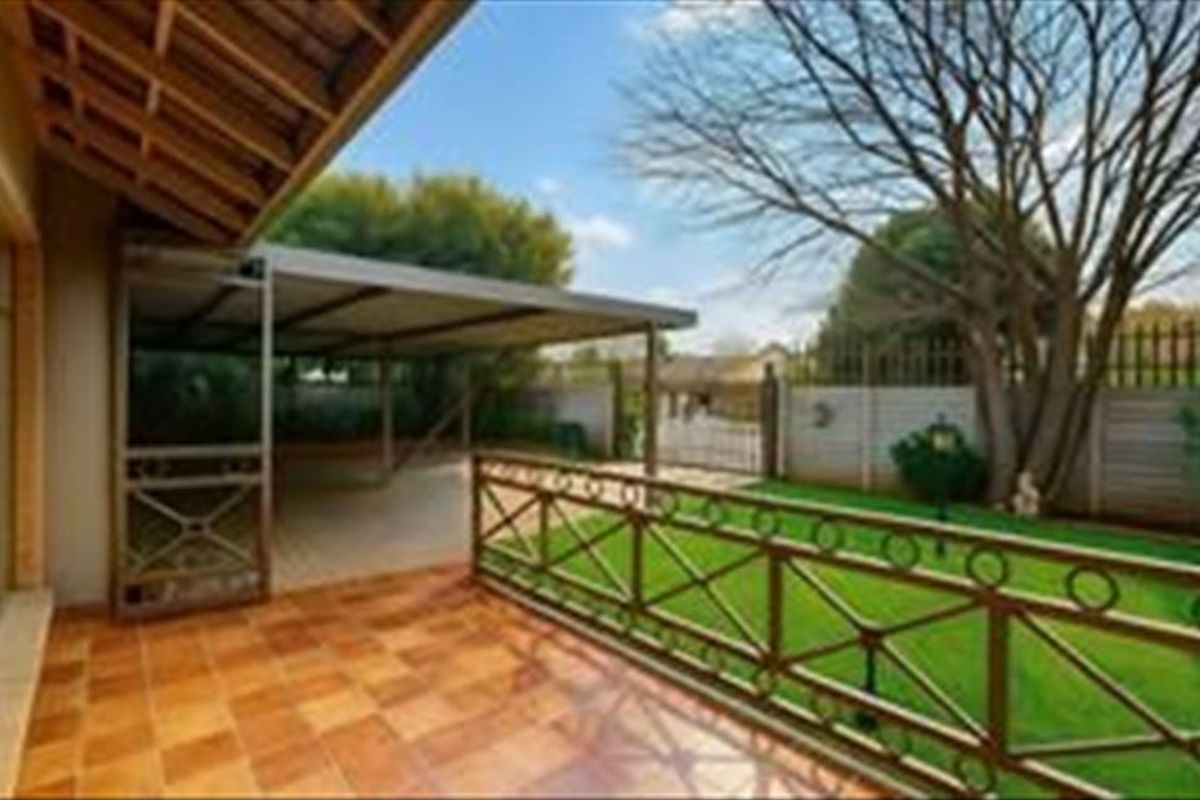 A covered patio area featuring terracotta tiling, overlooking a private garden with a lawn and a carport structure.