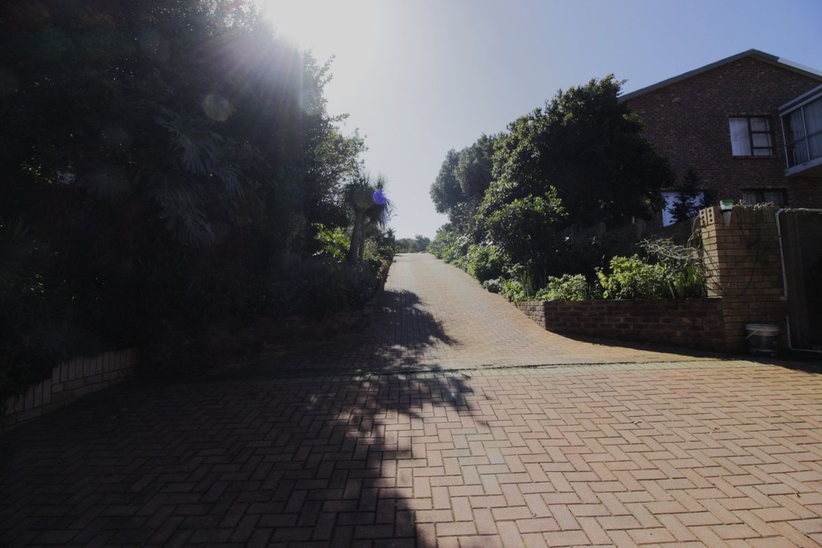 A view of a paved residential driveway leading upwards, flanked by established garden beds and a brick retaining wall.