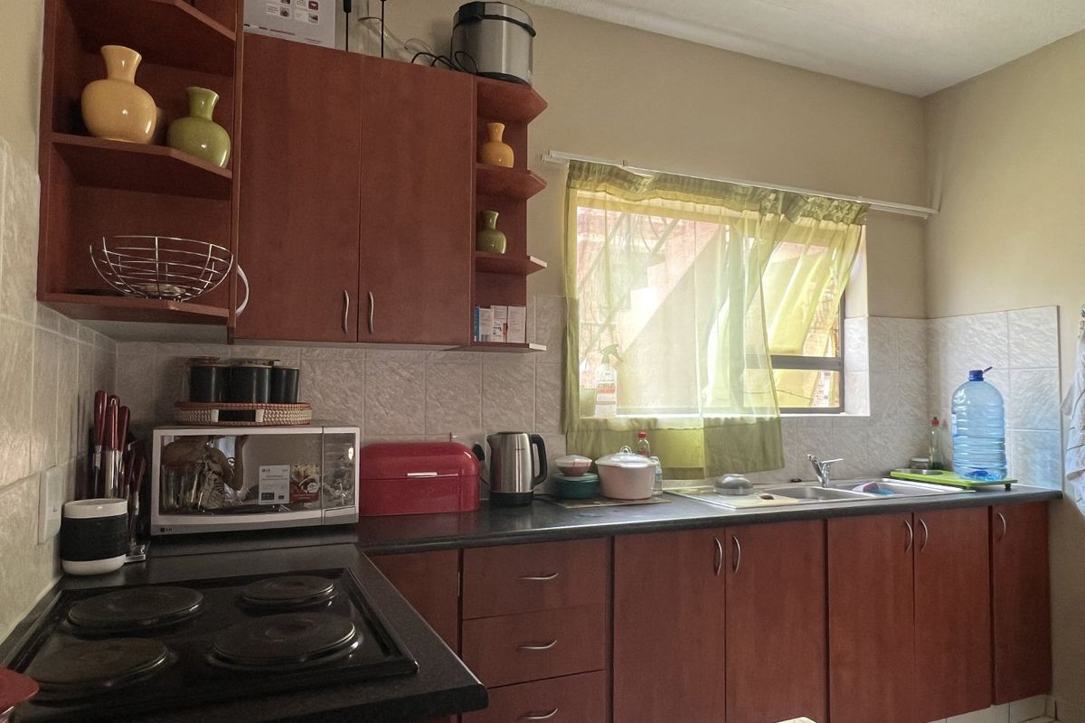 A functional kitchen featuring wood-tone cabinetry, dark laminate countertops, a built-in electric hob, and a tiled backsplash with a window for natural light.