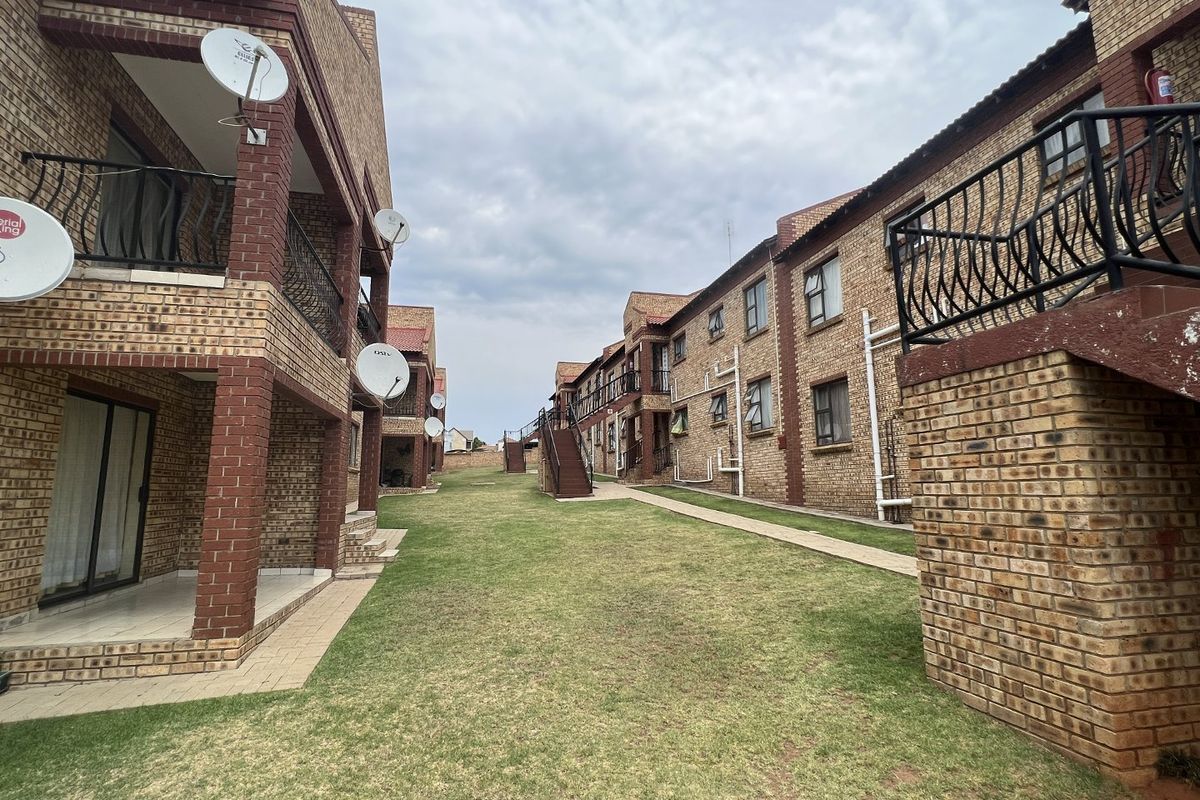 View of the communal garden area between apartment blocks, featuring face brick facades, paved walkways, and external staircases.