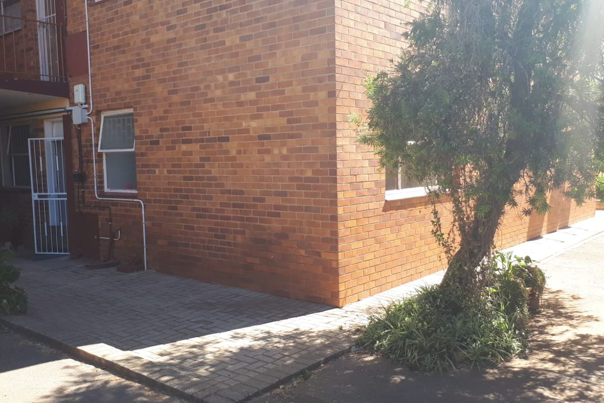 Exterior view of the apartment building featuring a brick facade, paved walkway, and security gate access.