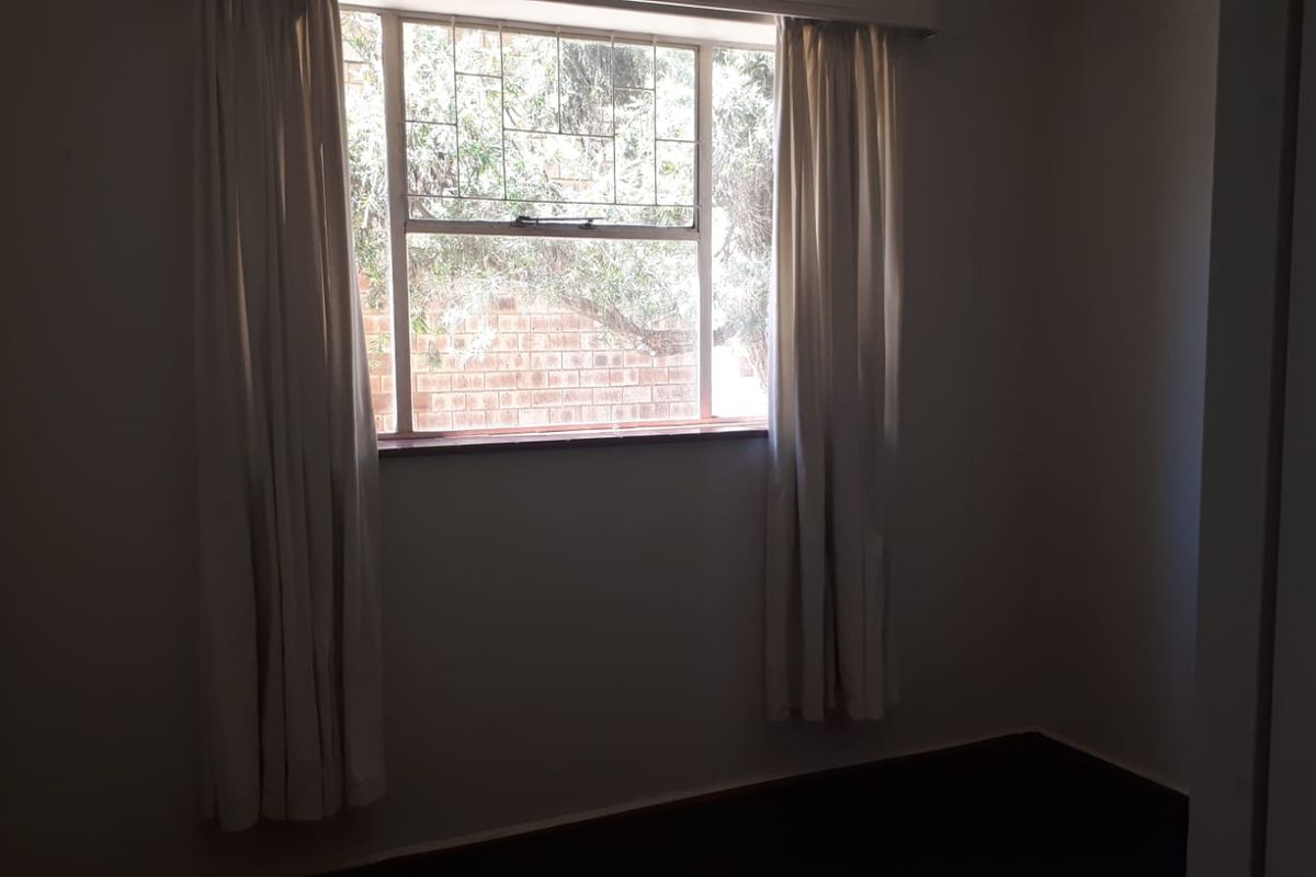A simple, empty bedroom featuring a window with security bars and curtain tracks, offering a blank canvas for interior design.