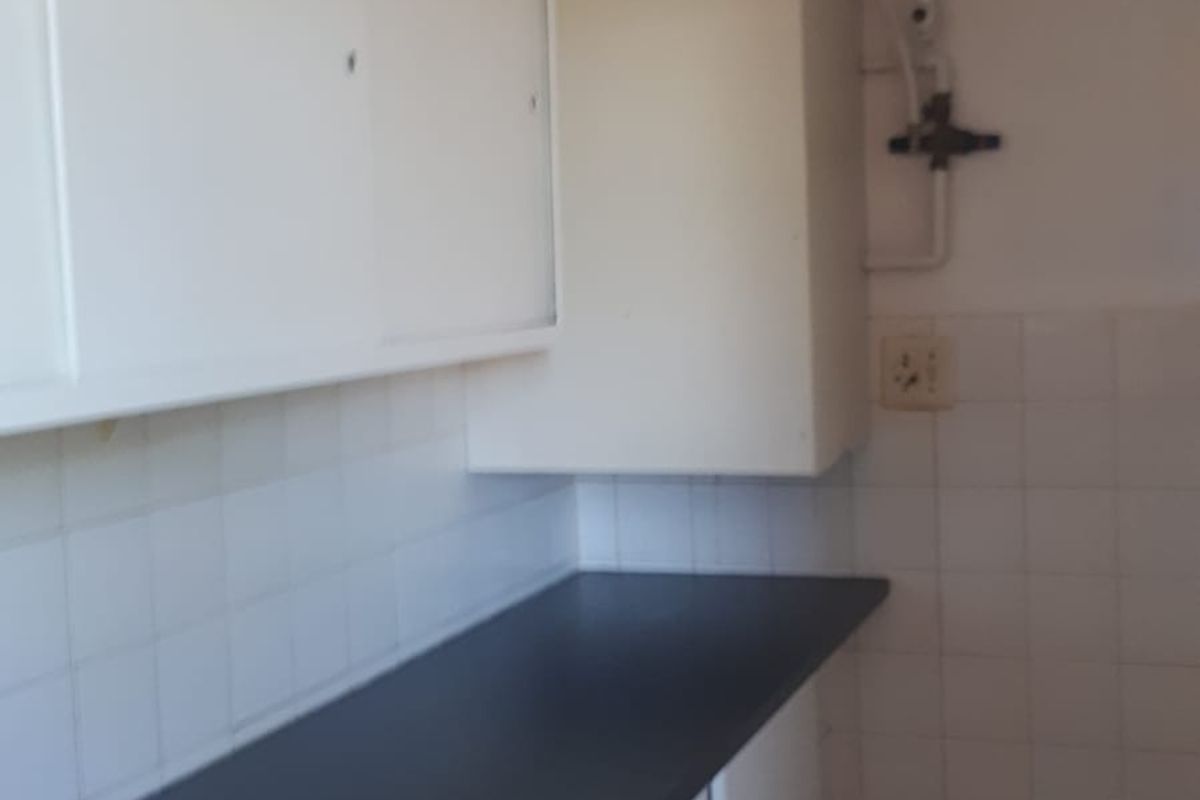 A compact kitchen area featuring white cabinetry, a dark laminate countertop, and tiled backsplash, currently in a dated condition.