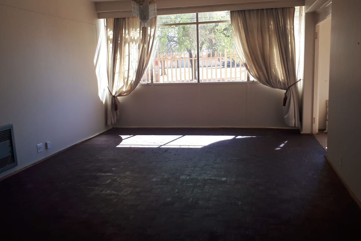 Spacious living room featuring original parquet flooring, a built-in wall heater, and large windows allowing for ample natural light.
