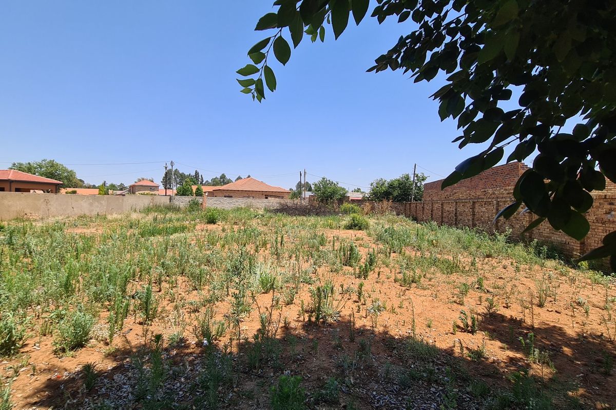 A vacant residential plot featuring perimeter brick boundary walls and natural ground cover, suitable for future development.