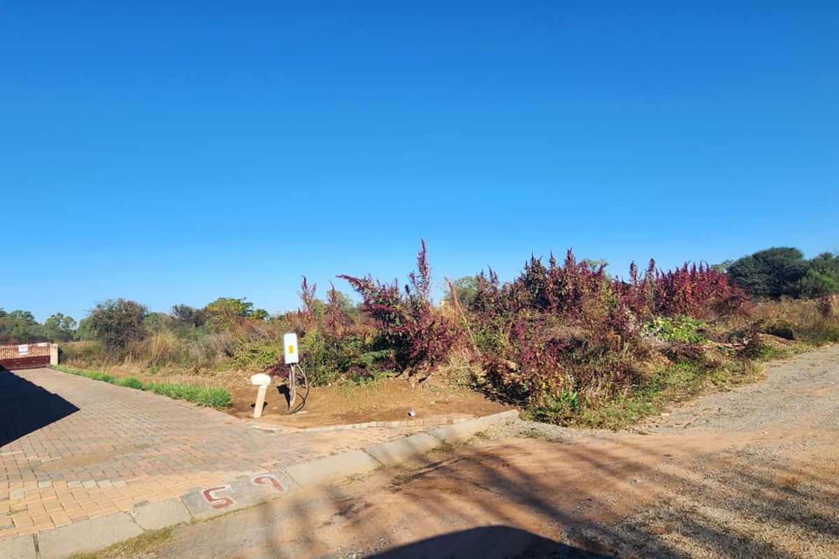 Vacant residential land featuring a paved driveway, brick boundary wall, and established electrical connection point, ready for development.