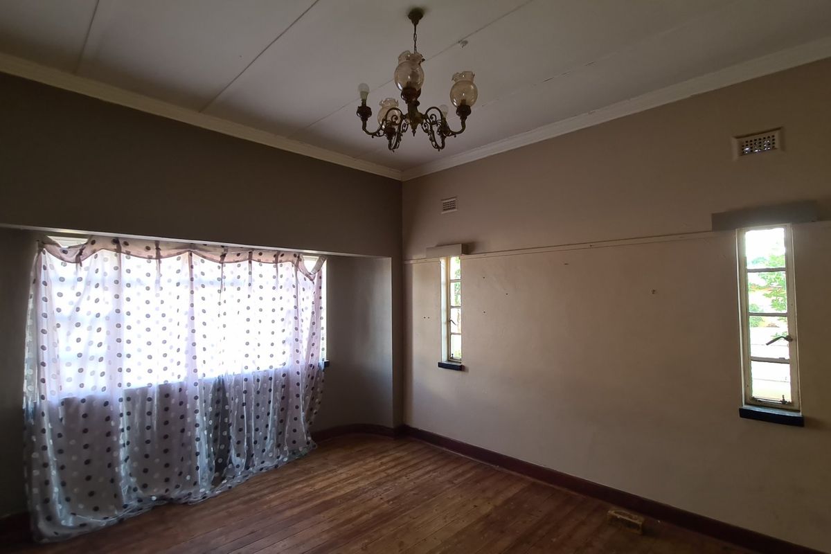 An empty living room featuring original hardwood flooring, a classic chandelier, and multiple windows providing natural light, ready for renovation and modernization.
