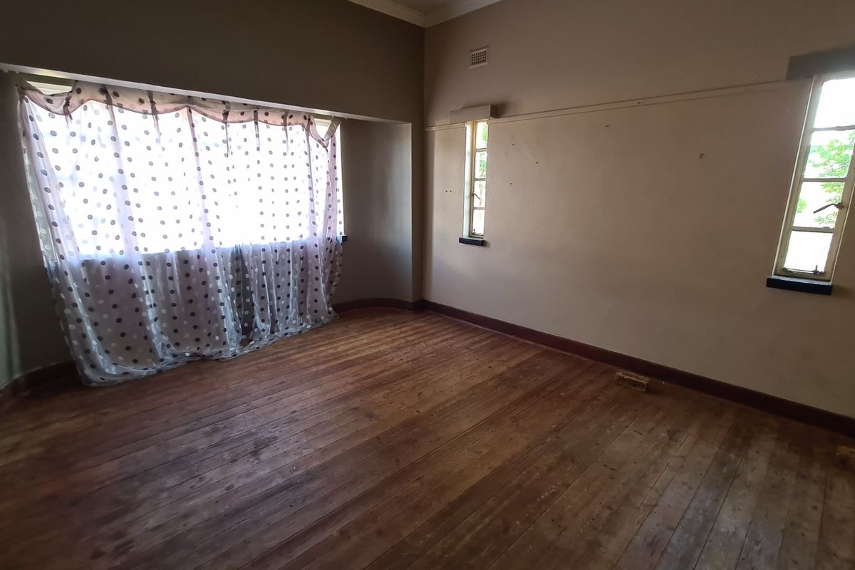 An empty bedroom featuring original timber flooring, multiple windows providing natural light, and neutral wall finishes ready for renovation.
