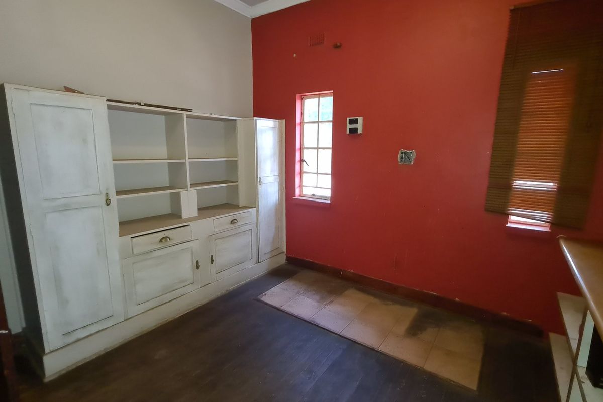 A vacant kitchen area featuring built-in cabinetry, red accent walls, and window blinds, requiring cosmetic updates and repairs to fixed finishes.