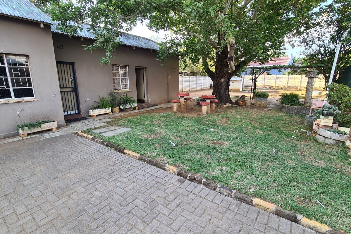 Rear exterior view of the house featuring a paved area, lawn, mature tree, and masonry wall construction with visible exterior wear.
