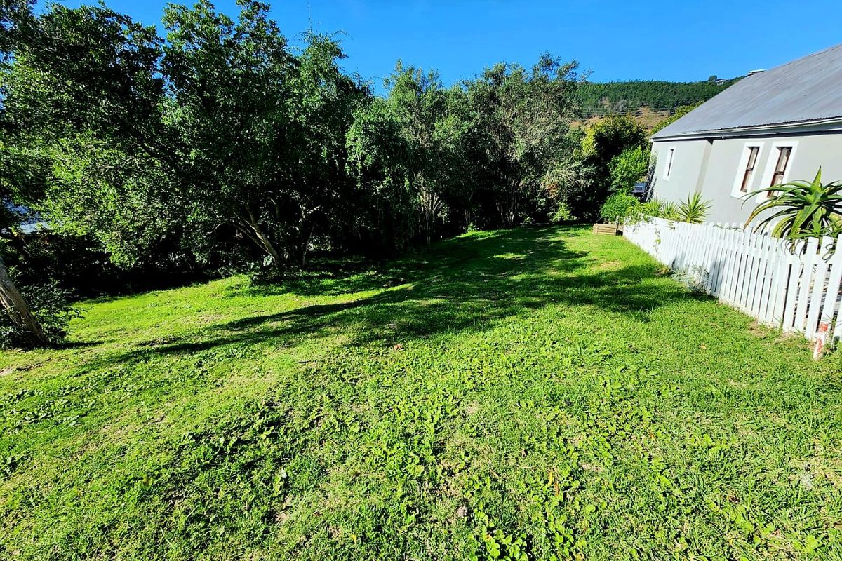 A spacious, well-maintained grassy garden area featuring mature trees and a white picket fence bordering the property.