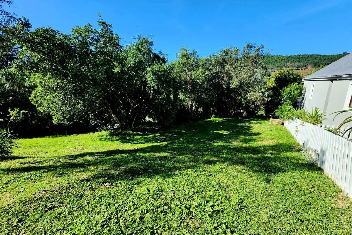 A spacious, well-maintained residential garden area featuring mature trees and a white picket fence boundary.