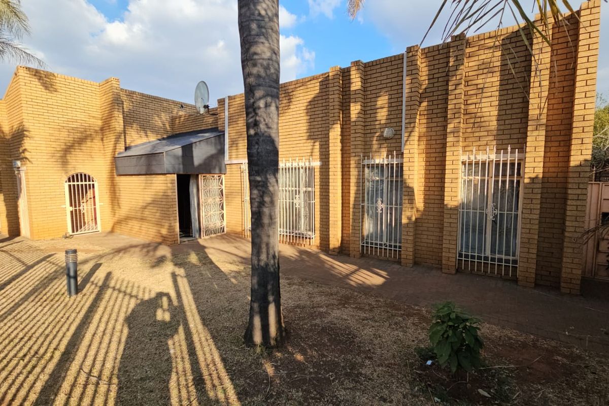 Rear exterior view of the house featuring face brick walls, security bars on windows, and a paved walkway area.