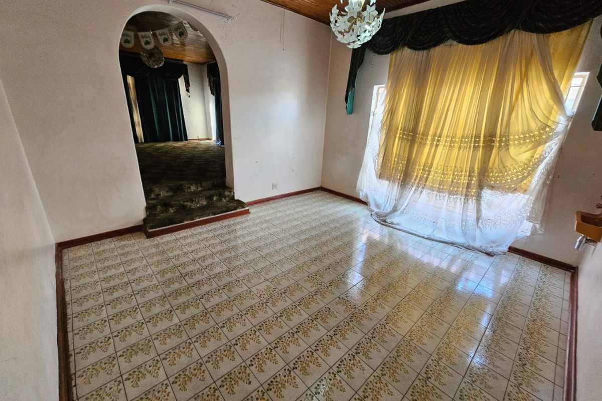 An empty living room featuring a raised platform, arched doorway, tiled flooring, and a timber ceiling, offering a dated interior ready for modernization.