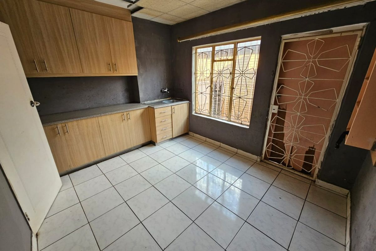 A kitchen space featuring laminate cabinetry, tiled flooring, and security fixtures, currently requiring ceiling repairs and cosmetic updates to improve its overall condition.
