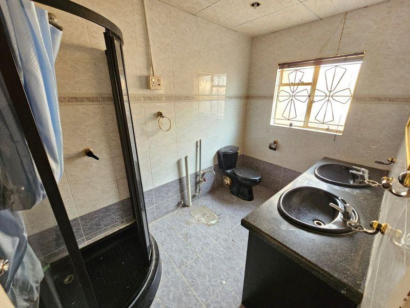 A bathroom featuring a shower enclosure, double vanity, and toilet. The space requires maintenance and cosmetic updates to improve its overall condition.
