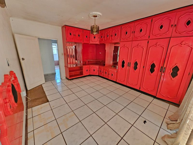 Spacious bedroom featuring extensive built-in cabinetry, ceramic tiled flooring, and a classic ceiling rose, offering a blank canvas for renovation and modernization.