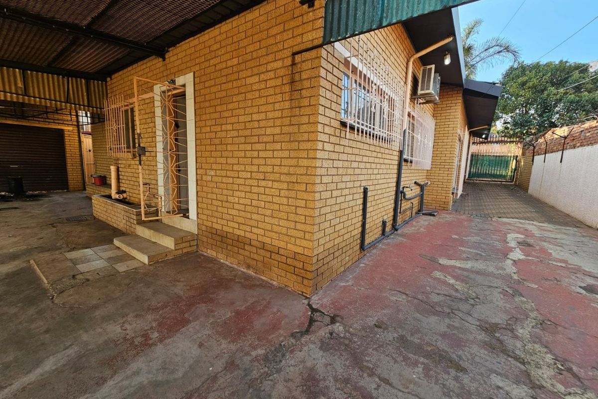 Rear exterior view of the property featuring face brick walls, security bars on windows, and a paved area with visible wear and tear.