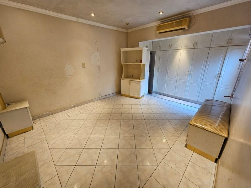 Spacious bedroom featuring extensive built-in cupboards, tiled flooring, and a wall-mounted air conditioning unit, requiring cosmetic wall repairs.