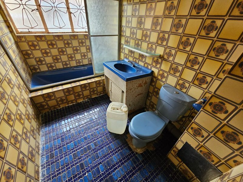 A dated bathroom featuring blue sanitaryware, patterned wall tiles, and a built-in bathtub, requiring modernization to improve its aesthetic and functional appeal.
