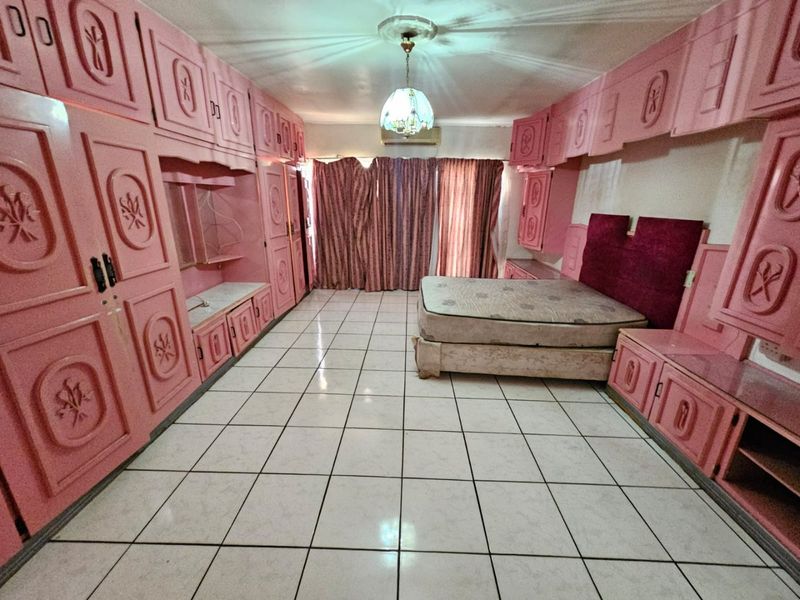 Spacious bedroom featuring extensive built-in cabinetry, tiled flooring, and an integrated air conditioning unit, offering significant potential for modernization.