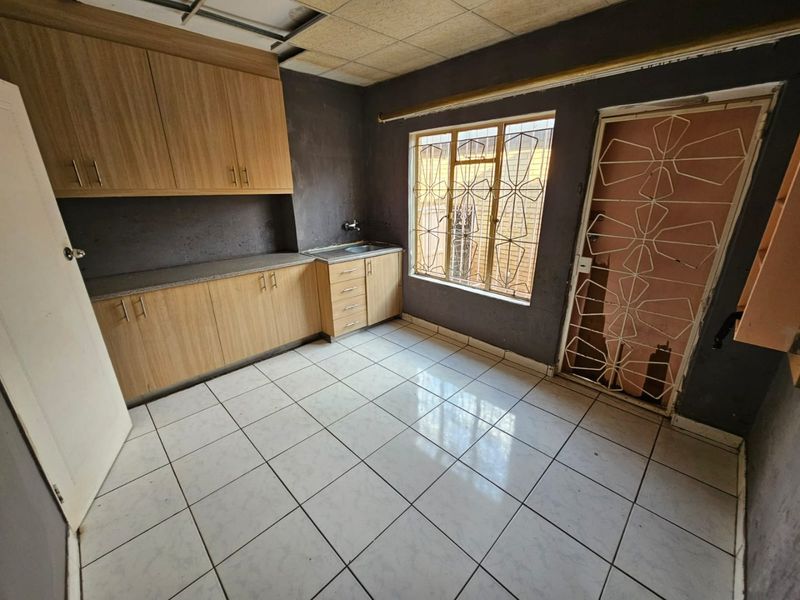 A basic kitchen area featuring built-in cabinetry, tiled flooring, and security fixtures, currently requiring ceiling repairs and cosmetic updates.