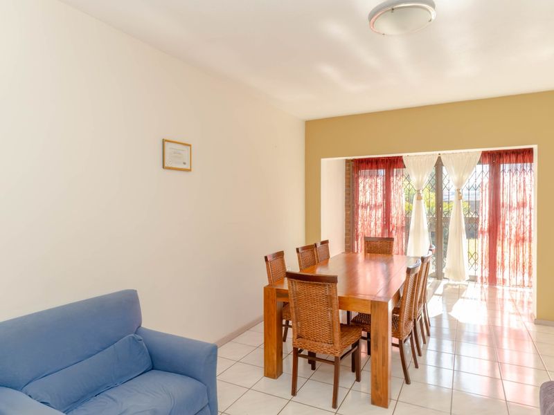 A dining area featuring ceramic floor tiles and a sliding glass door with security gate, providing access to the outdoor space.