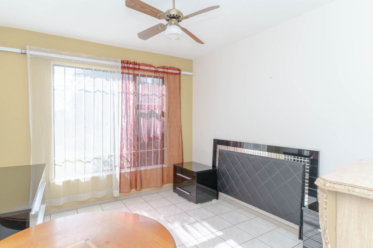 A bedroom featuring tiled flooring, a ceiling fan, and a window fitted with security bars.