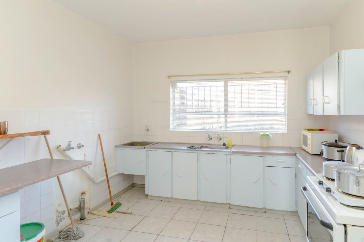 A functional kitchen featuring tiled flooring, built-in cabinetry, a stainless steel sink, and a tiled splashback, requiring cosmetic updates to modernize the space.