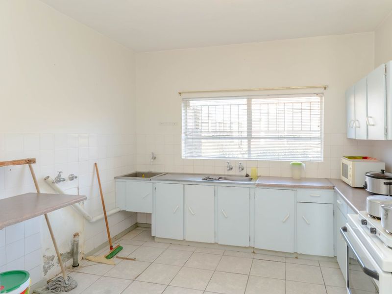 A functional kitchen featuring tiled flooring, built-in cabinetry, a stainless steel sink, and a tiled splashback, requiring cosmetic updates to modernize the space.