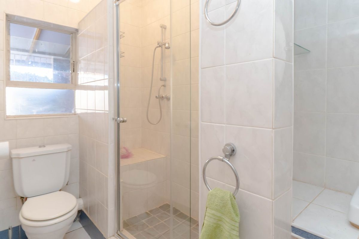 A functional bathroom featuring a glass-enclosed shower, white ceramic toilet, and neutral wall tiling throughout.