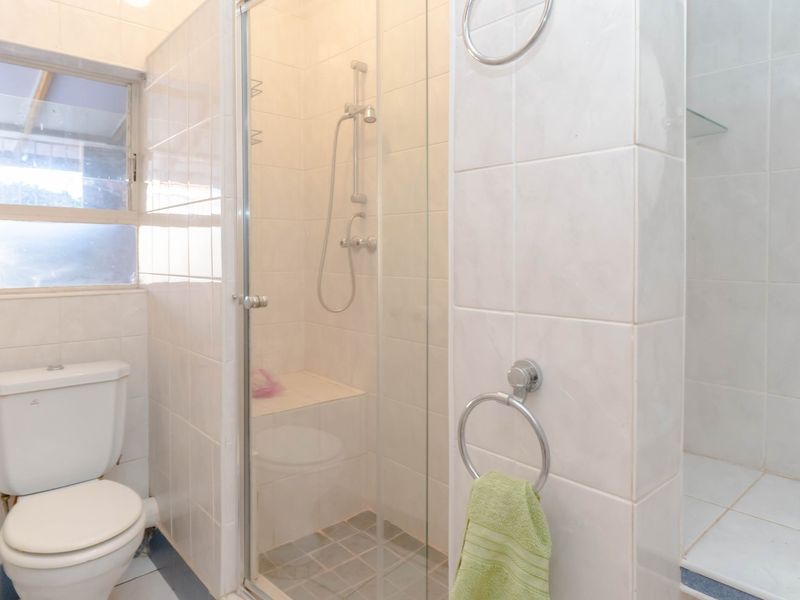 A functional bathroom featuring a glass-enclosed shower, white ceramic toilet, and neutral wall tiling throughout.