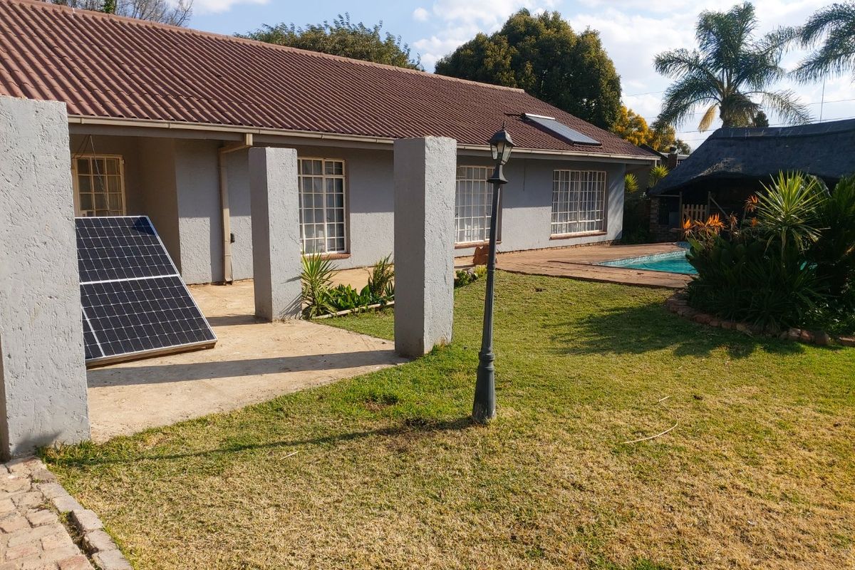 Rear exterior view featuring a tiled roof house, swimming pool, garden, and a thatched lapa area.