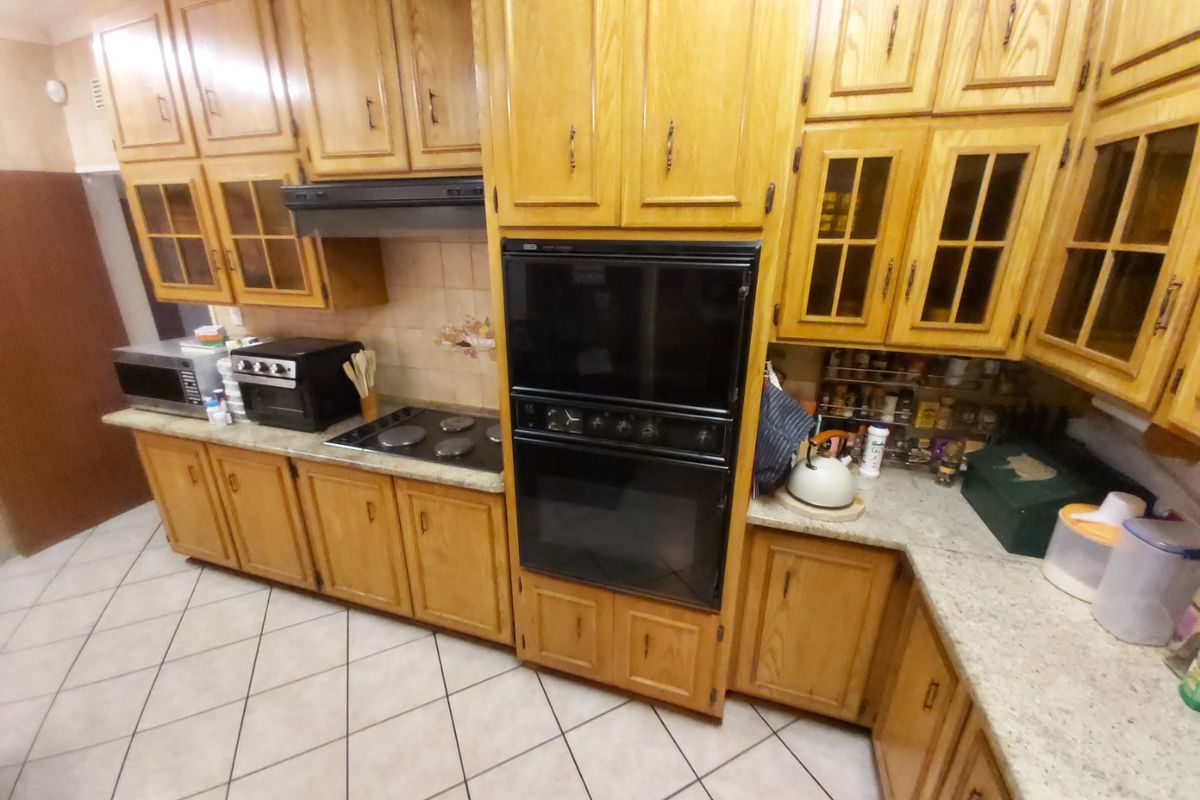 A functional kitchen featuring traditional wooden cabinetry, built-in double oven, electric hob, and tiled flooring with ample counter space.