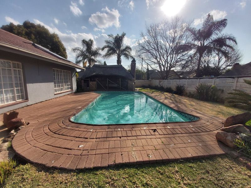 Outdoor pool area featuring a swimming pool, brick paved surround, and a thatched lapa, set within a private garden with perimeter walling.