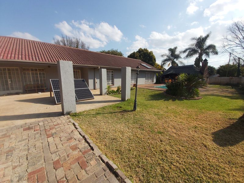 Rear exterior view featuring a tiled roof house, swimming pool, thatched lapa, and a brick-paved patio area with solar panels.